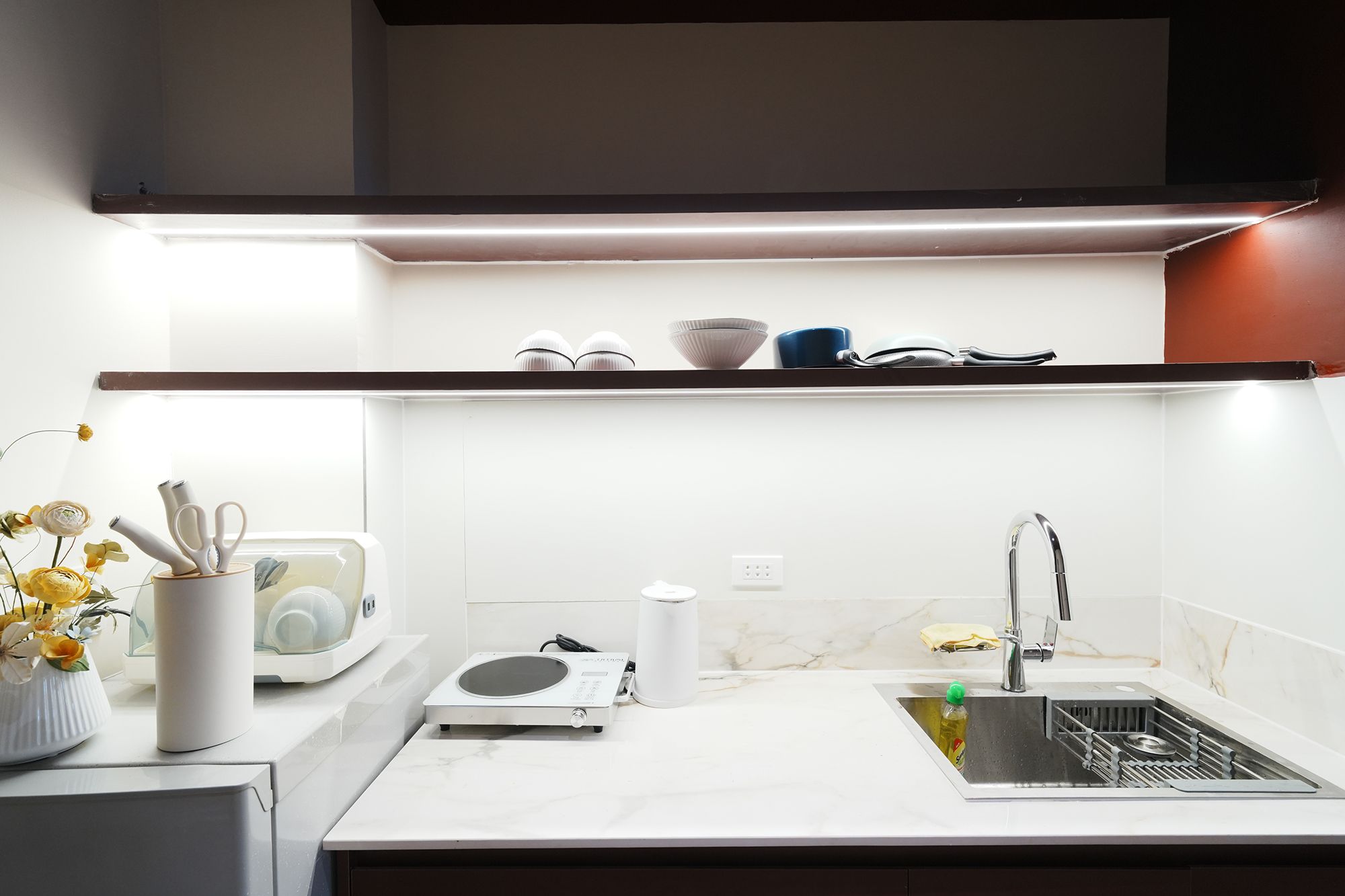 Uma cozinha moderna com forno embutido, pia com escorredor de louça e bancada com cafeteira e um vaso de flores.