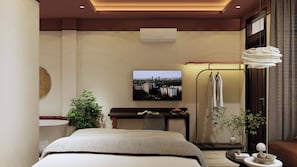 Quarto de hotel com cama, televisão na parede, secretária com planta e casa de banho com chuveiro e porta-toalhas.