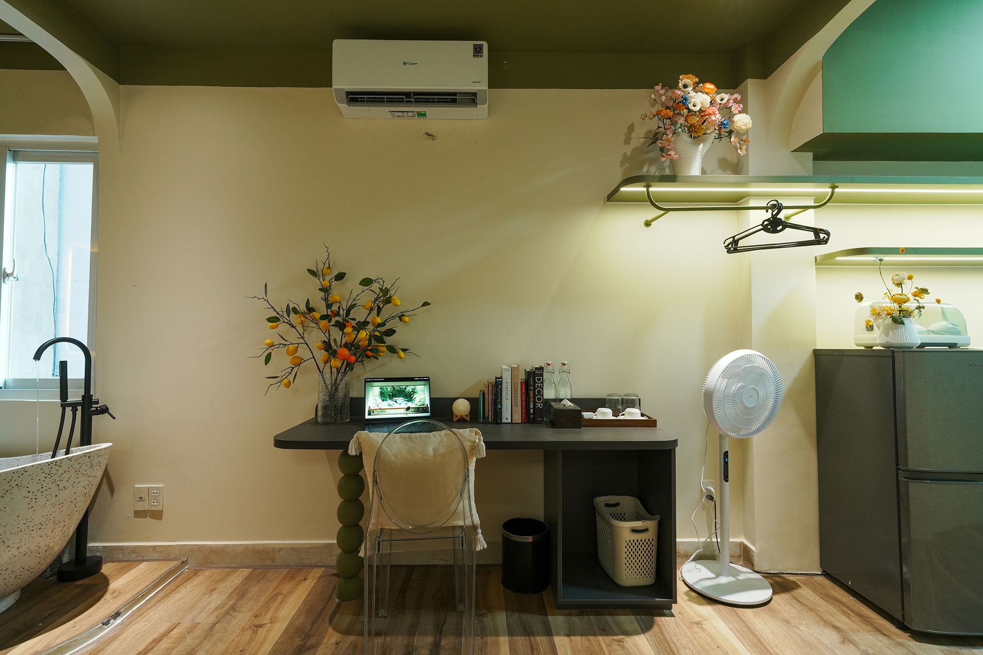 Cozinha equipada com ar condicionado, um laptop em uma mesa, um vaso com flores, um ventilador e uma geladeira.