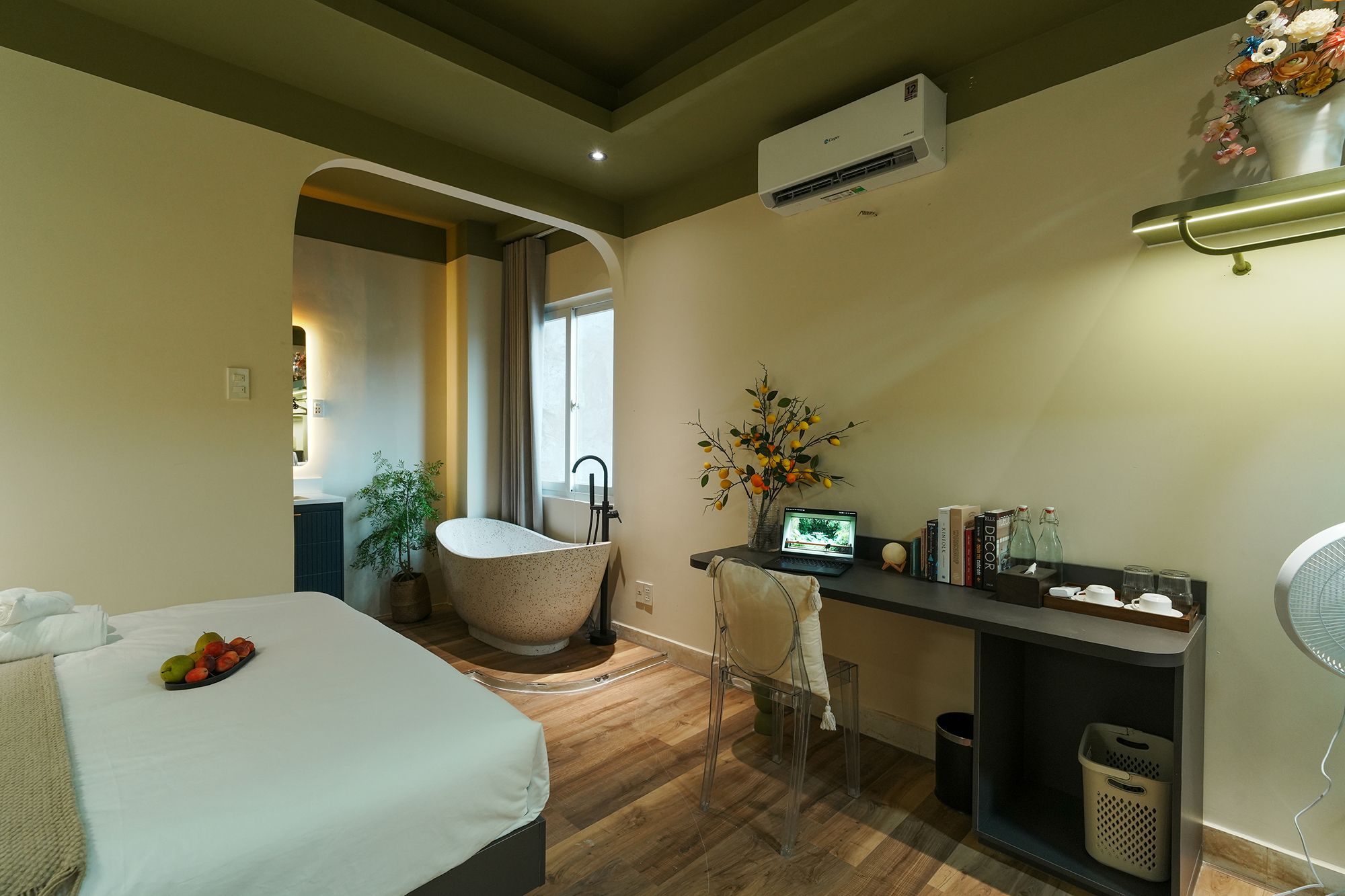 A hotel room with a bed, a desk with a laptop, a bathtub, and a small window.