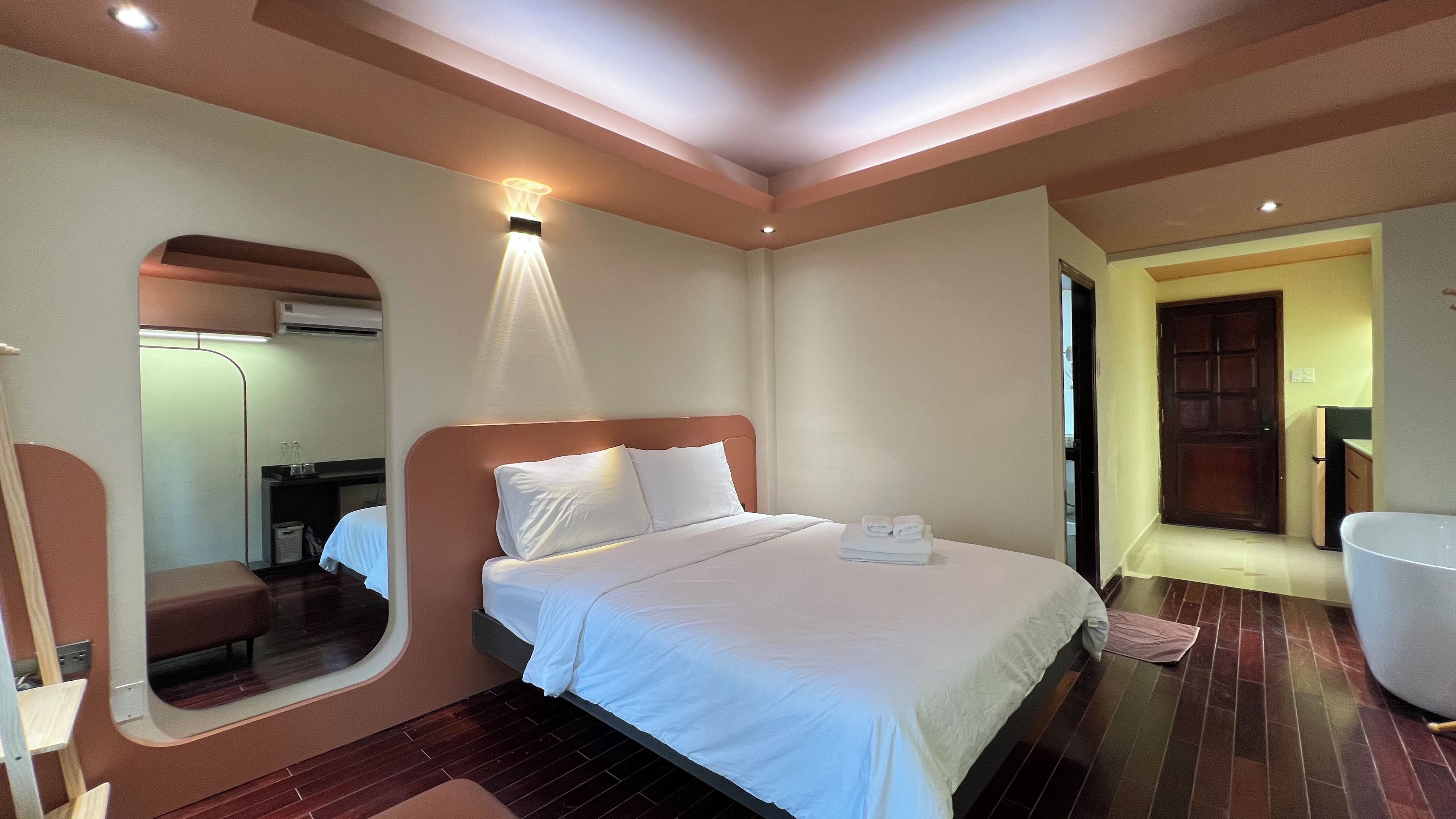 A hotel room with a bed, a mirror, a bedside table, a chair, and a door leading to a bathroom.