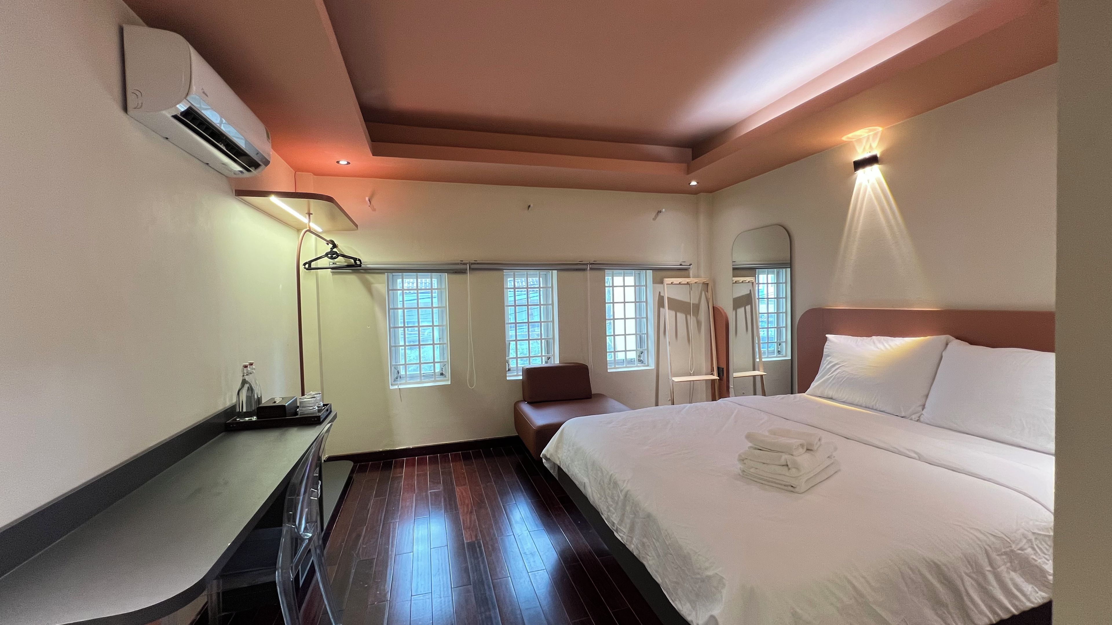 A hotel room with a bed, bedside table, chair, and a desk with a lamp.