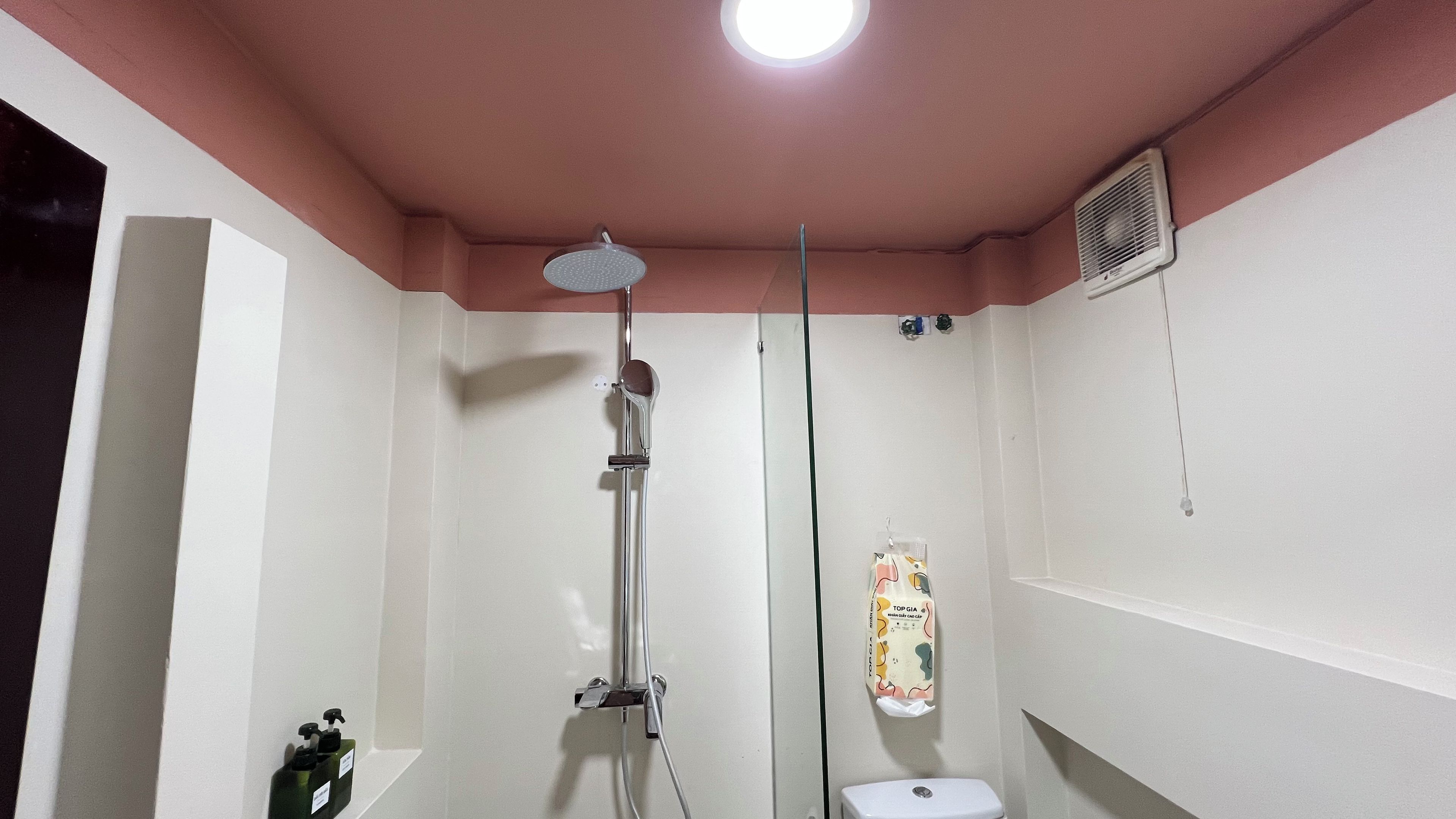 A bathroom with a shower, toilet, and a bottle of shampoo on the wall.