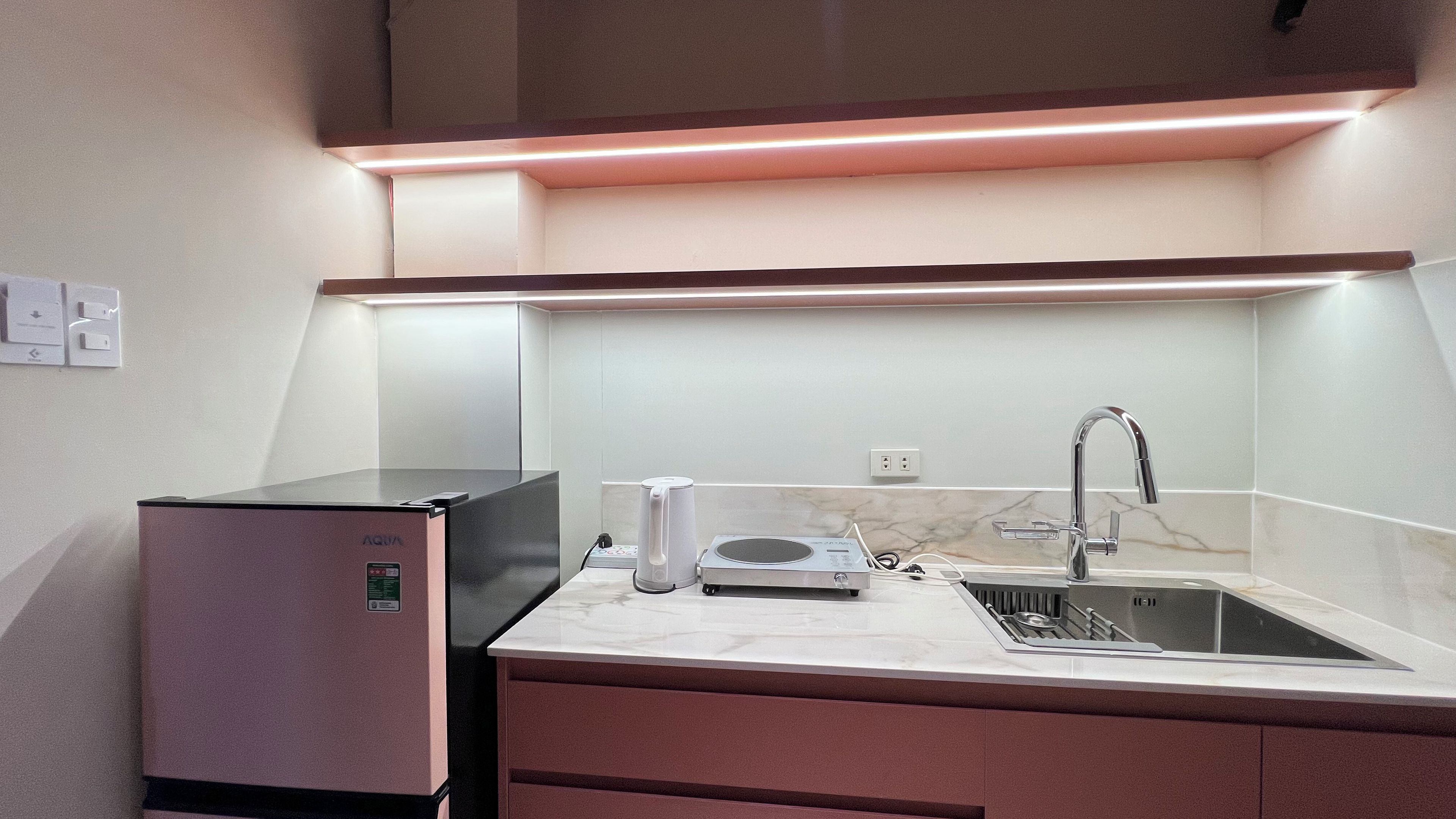 A compact kitchen with a built-in refrigerator, a microwave, a sink, and a coffee maker.