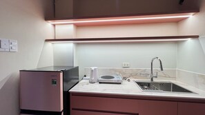 A compact kitchen with a built-in refrigerator, a microwave, a sink, and a coffee maker. - PIN Truong Quyen (Ho Chi Minh City)