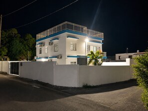 A two-story building with a balcony on the upper floor, surrounded by a low wall and a palm tree. - Kardo Villa, 6 Bedrooms, Private Pool & Tropical Escape (Pointe-aux-Sables)