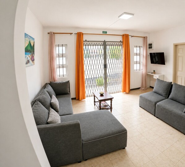 A modern living room with grey sofas, a coffee table, and a TV mounted on the wall. - Kardo Villa, 6 Bedrooms, Private Pool & Tropical Escape (Pointe-aux-Sables)