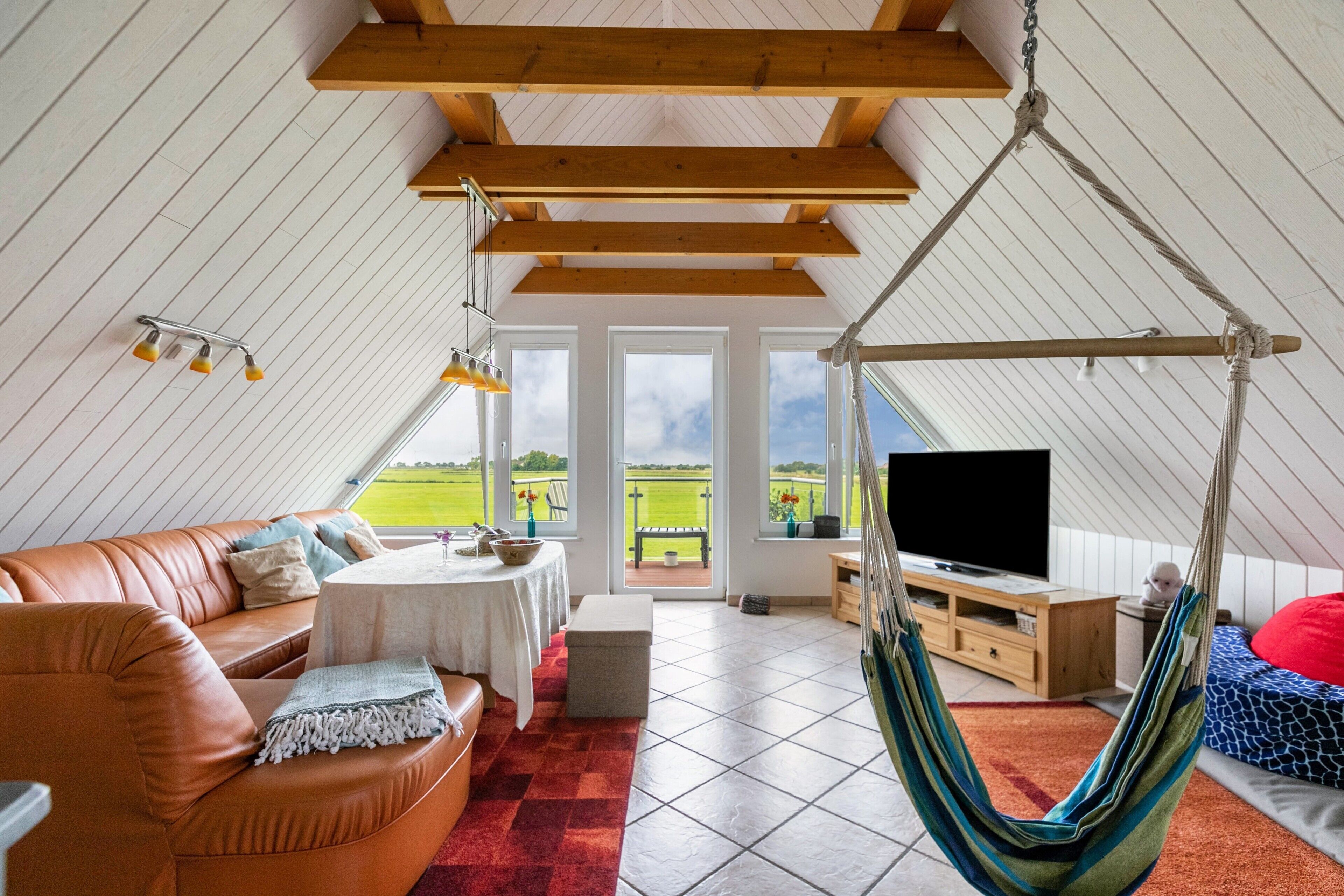 Um quarto espaçoso com teto alto, uma cadeira suspensa, um sofá, uma televisão e vista para o exterior.