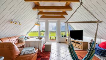 Um quarto espaçoso com teto alto, uma cadeira suspensa, um sofá, uma televisão e vista para o exterior.