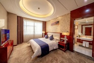 Habitación de hotel con una cama grande, una mesita de noche, un televisor y un baño con espejo y lavabo.