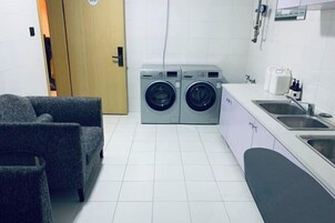 Una cocina compacta con lavadora, un lavamanos y una silla.