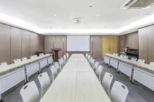 Un salón de conferencias con una larga mesa, sillas, un atril y una pantalla de proyector.