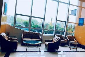 A lobby with a large window, leather sofas, a small round table, and a wall-mounted information board.