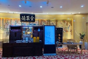 A hotel lobby with a reception desk, a digital display, and a seating area.