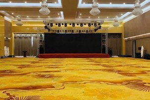 Un amplio salón con alfombra, un escenario, candelabros y una alfombra roja.