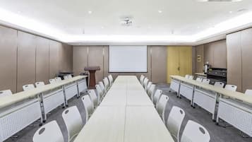 Un salón de conferencias con una larga mesa, sillas, un atril y una pantalla de proyección.