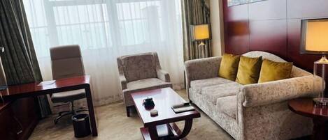 A hotel room with a sofa, armchair, coffee table, desk, and lamps.
