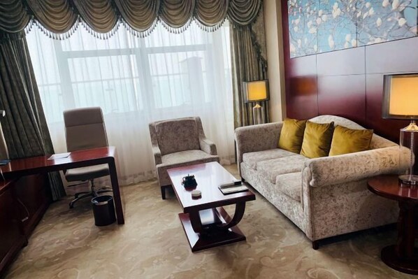 A hotel room with a sofa, armchair, coffee table, desk, and lamps.