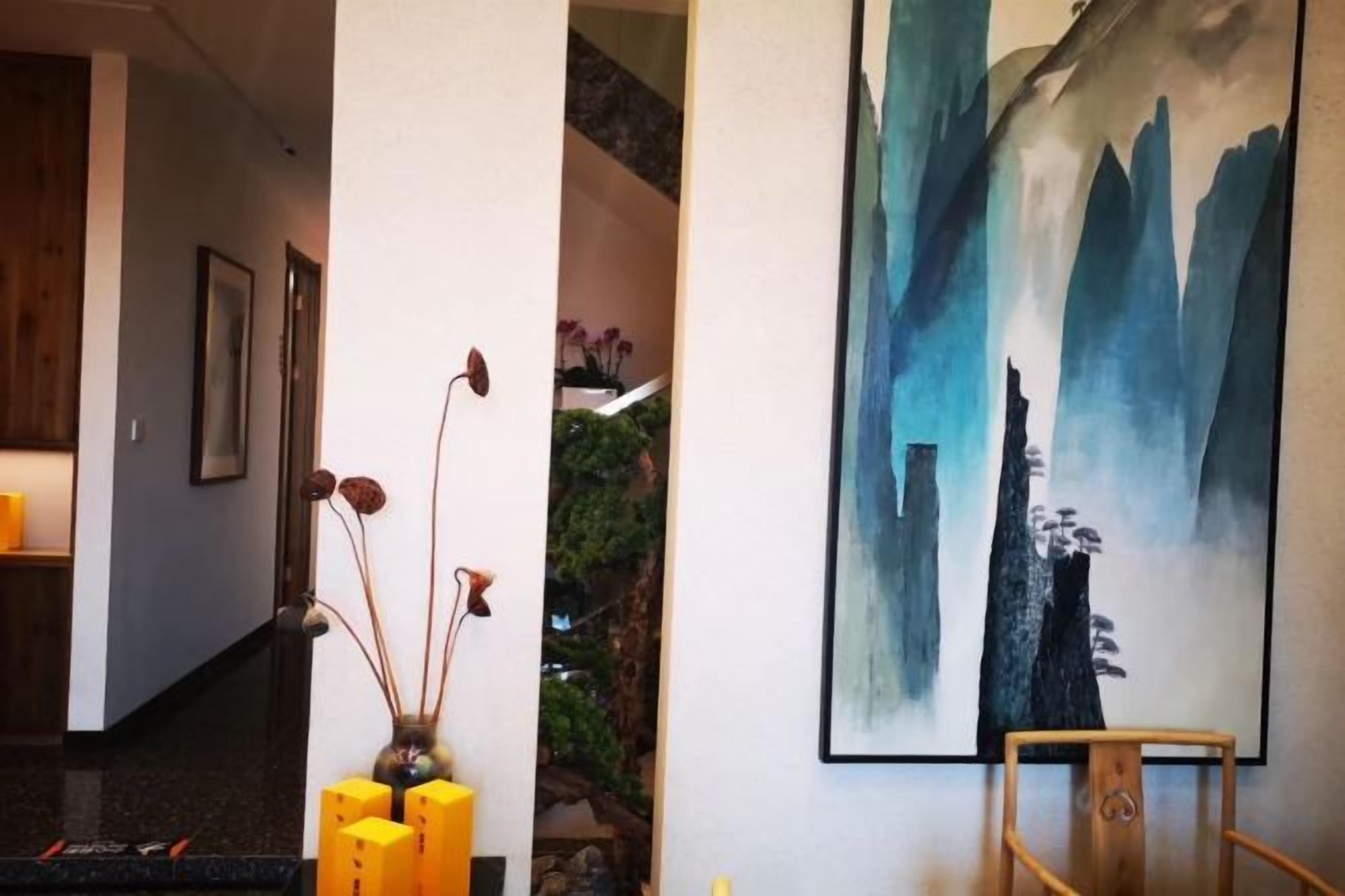 Un couloir avec un escalier, un tableau représentant un paysage de montagne et un vase contenant des fleurs séchées.