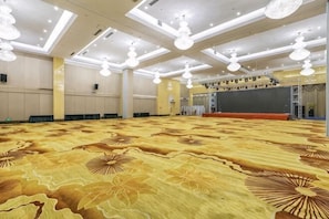 A large conference room with a patterned carpet, a stage, and ceiling lights.