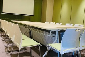 A conference room with a long table and chairs, a projector screen, and a green wall.