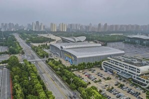 A large, modern building with a curved roof, surrounded by a parking lot and a road. - Cangzhou Bohai Hotel (Cangzhou)