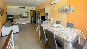 A modern kitchen with white cabinets, a dining area with a marble table, and a living room with a sofa. - FranSea House (Otranto)