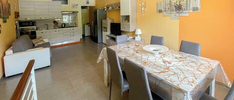 A modern kitchen with white cabinets, a dining area with a marble table, and a living room with a sofa.