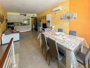 Eine moderne Küche mit weißen Schränken, ein Essbereich mit einem Marmortisch und ein Wohnzimmer mit einer Couch.