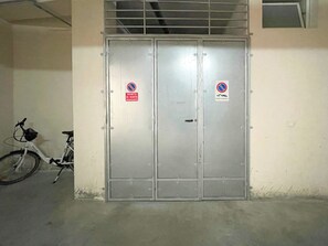 Eine Metall-Doppeltür mit zwei Schildern, eines verboten das Parken, das andere das Parken von Autos. Ein Fahrrad ist links von der Tür abgestellt.