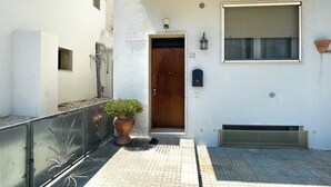 A building entrance with a wooden door, a mailbox, a potted plant, and a window with a shutter. - FranSea House (Otranto)