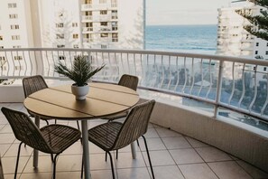 A round table with four chairs and a potted plant on a balcony with a view of the sea and buildings. - Biarritz by the Sea | Resort Days & Ocean Views (Gold Coast)