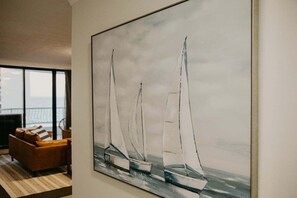 A painting of sailboats on a wall in a room with a sofa and a view through a window. - Biarritz by the Sea | Resort Days & Ocean Views (Gold Coast)
