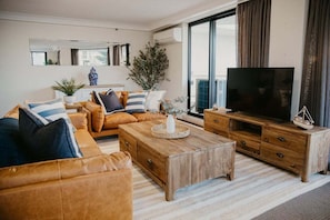 A modern living room with a sofa set, a coffee table, a TV, and a wooden cabinet. - Biarritz by the Sea | Resort Days & Ocean Views (Gold Coast)