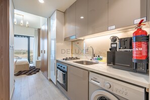 A modern kitchen with a built-in dishwasher, a stove, and a microwave. - Stylish Studio Retreat with Balcony Overlooking Serene Community Views (Dubai)