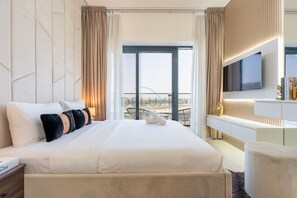 A hotel room with a large bed, a TV, a desk, and a view of the beach. - Stylish Studio Retreat with Balcony Overlooking Serene Community Views (Dubai)