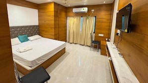 A bedroom with a bed, a chair, a TV, and an air conditioning unit.
