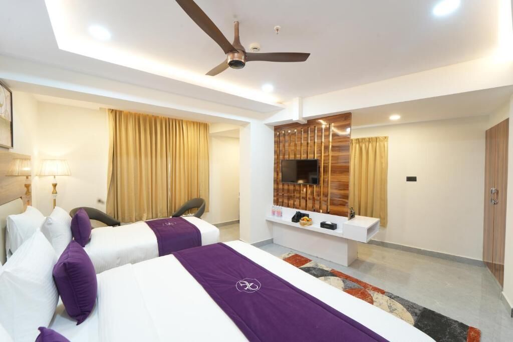 A hotel room with two beds, a desk, a television, and a ceiling fan.