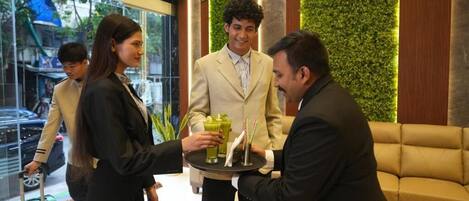 A reception area with a green wall, a sofa, and a person holding a tray with drinks.