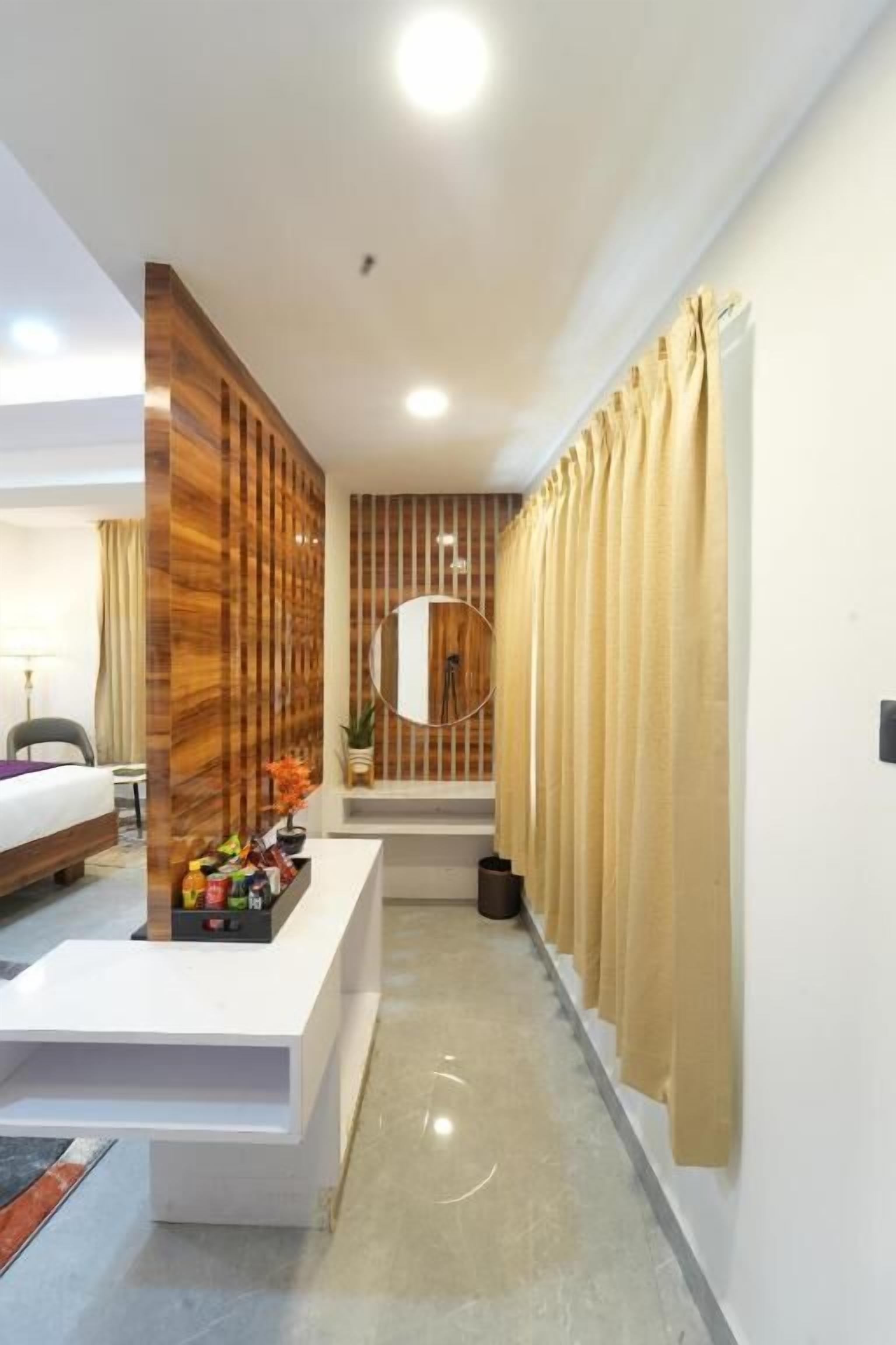 A modern hotel room with a wooden accent wall, a white reception desk, and a view of the hallway.