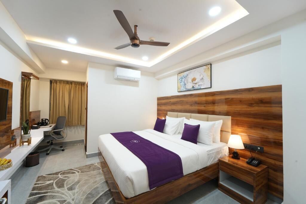 Una habitación de hotel con cama, mesita de noche, escritorio, silla y ventilador de techo.