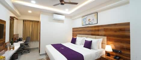 Una habitación de hotel con cama, mesita de noche, escritorio, silla y ventilador de techo.