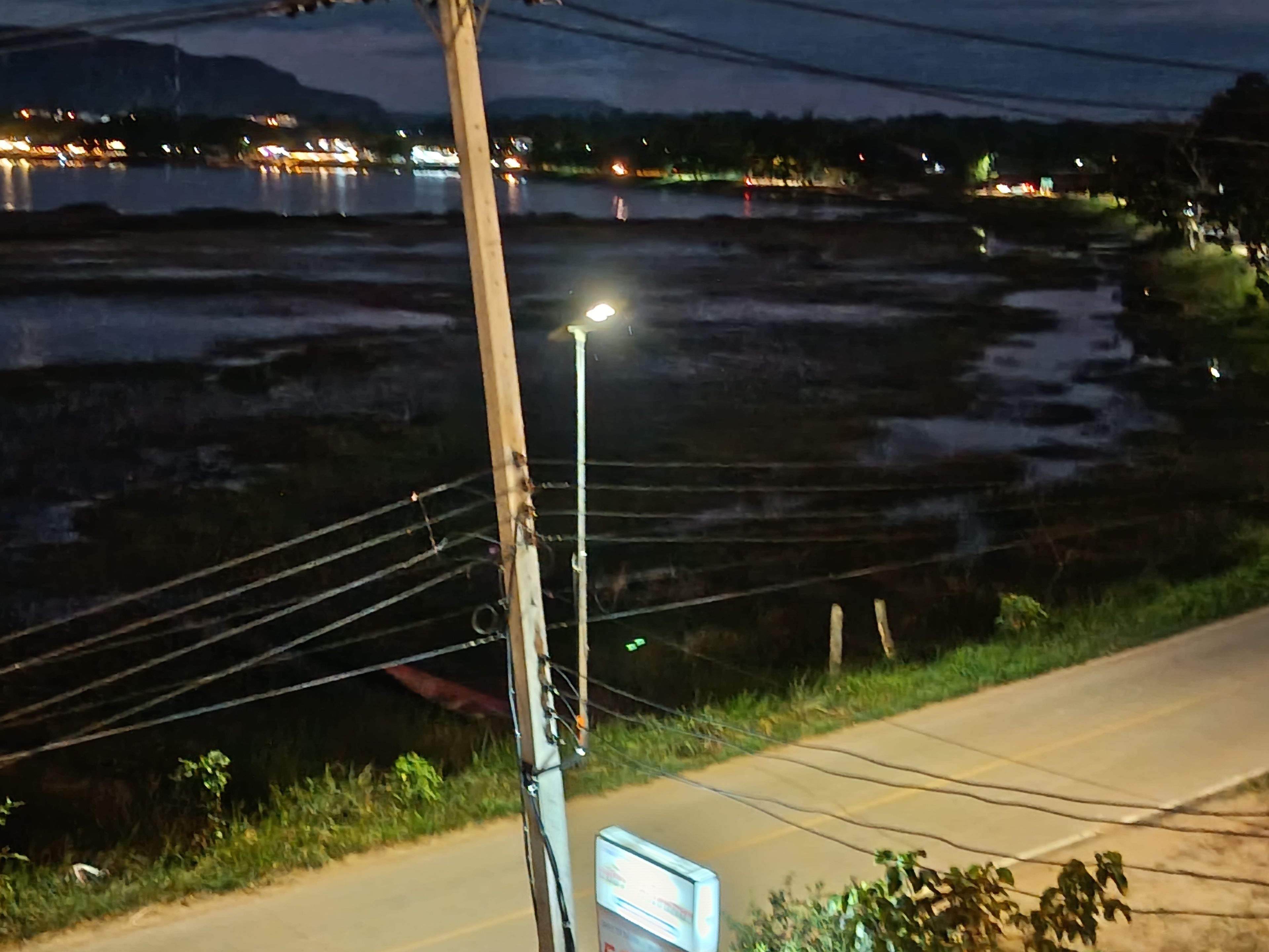 A nighttime view of a rural area with a road, a utility pole, and a body of water in the background.