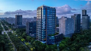 A high-rise building with a modern glass facade, surrounded by other high-rise buildings and greenery.