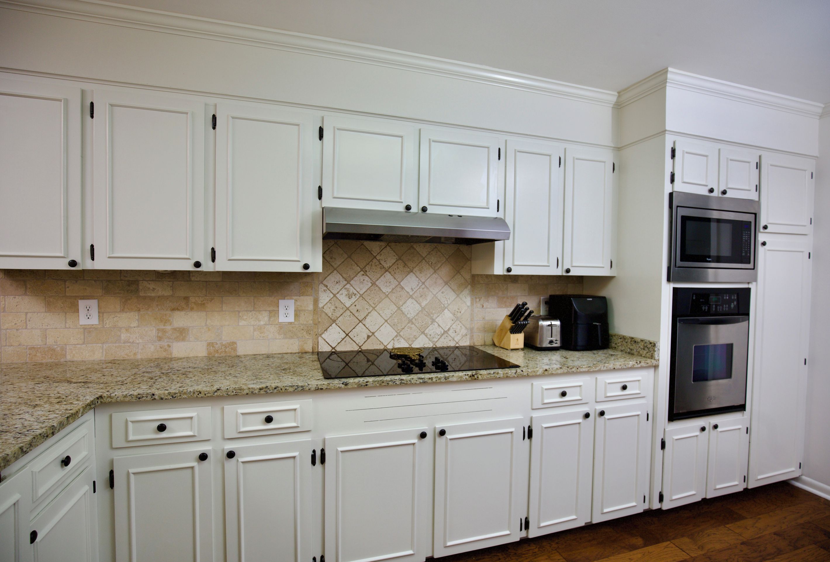 A kitchen with white cabinets, a stainless steel oven, a microwave, and a granite countertop.