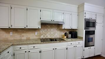 A kitchen with white cabinets, a stainless steel oven, a microwave, and a granite countertop.