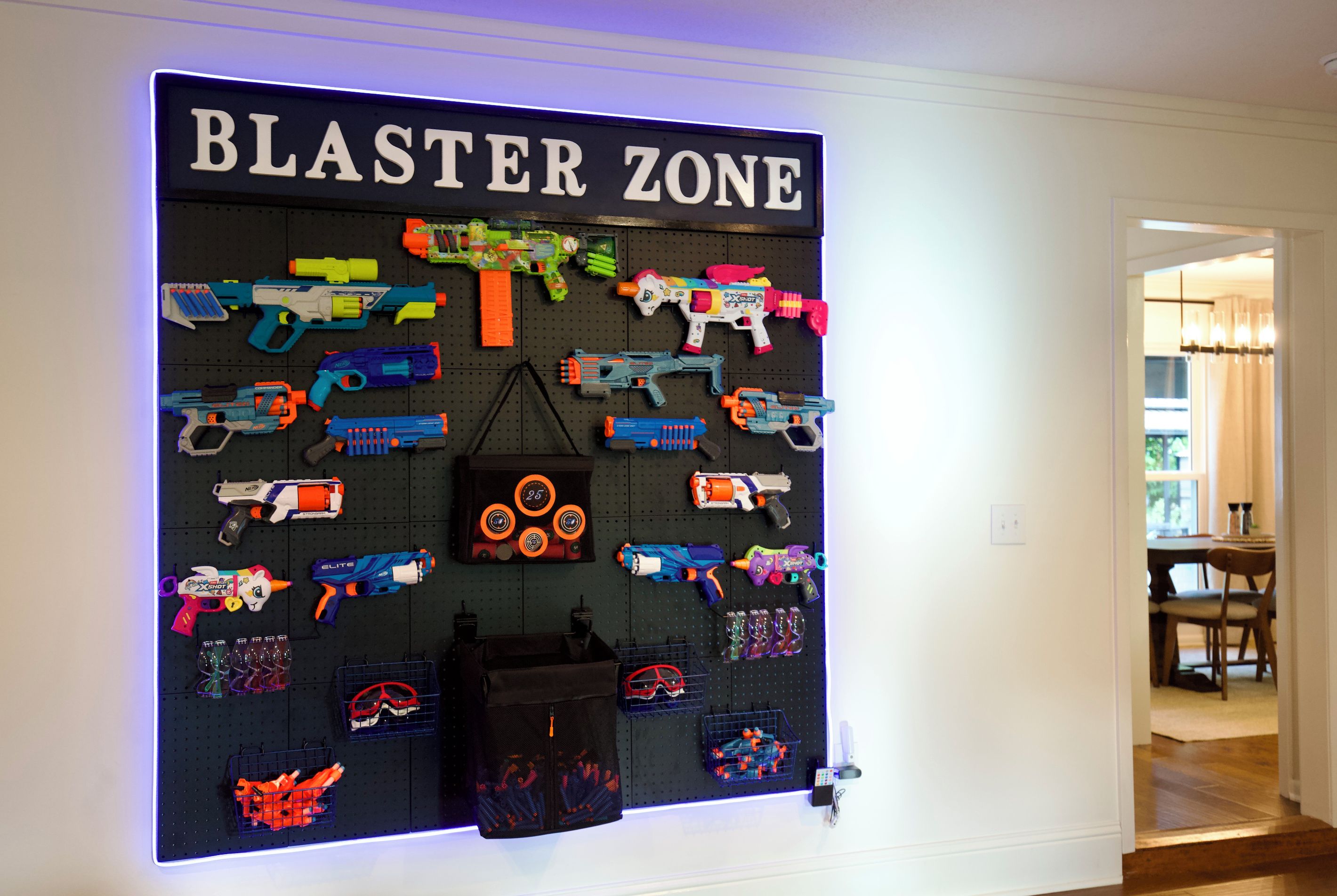 En väggmonterad utställning med olika typer av leksakspistoler och tillbehör, märkt med texten ”BLASTER ZONE”, och utformad med ett system av hålbrädor.