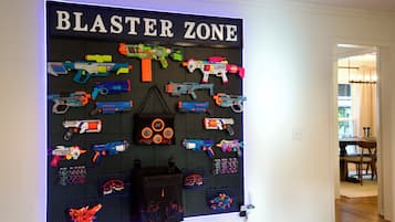 En väggmonterad utställning med olika typer av leksakspistoler och tillbehör, märkt med texten ”BLASTER ZONE”, och utformad med ett system av hålbrädor.