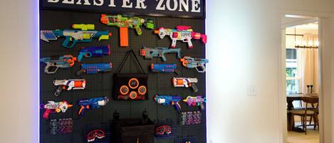 Una exhibición mural de varios blasters y accesorios de juguete, con la etiqueta 'BLASTER ZONE', con un diseño de tablero de aguja.