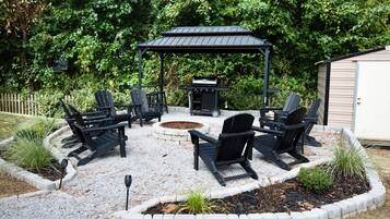 A circular outdoor seating area with Adirondack chairs and a fire pit, surrounded by a gravel patio and a stone border.